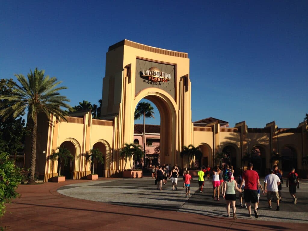 Entrada do parque de diversões Universal Studios Florida, com seus arcos amarelos clássicos, e pessoas chegando para um dia de diversões.