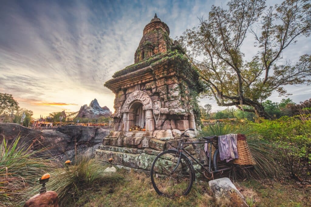 Foto artística que mostra uma áreas temáticas do parque Animal Kingdom, na Disney. Nessa imagem podemos ver o sol se pondo ao fundo, bem atrás do Everest, onde fica a montanha russa Expedition Everest, e mais a frente temos uma escultura e uma bicicleta fazendo a ambientação da áerea.
