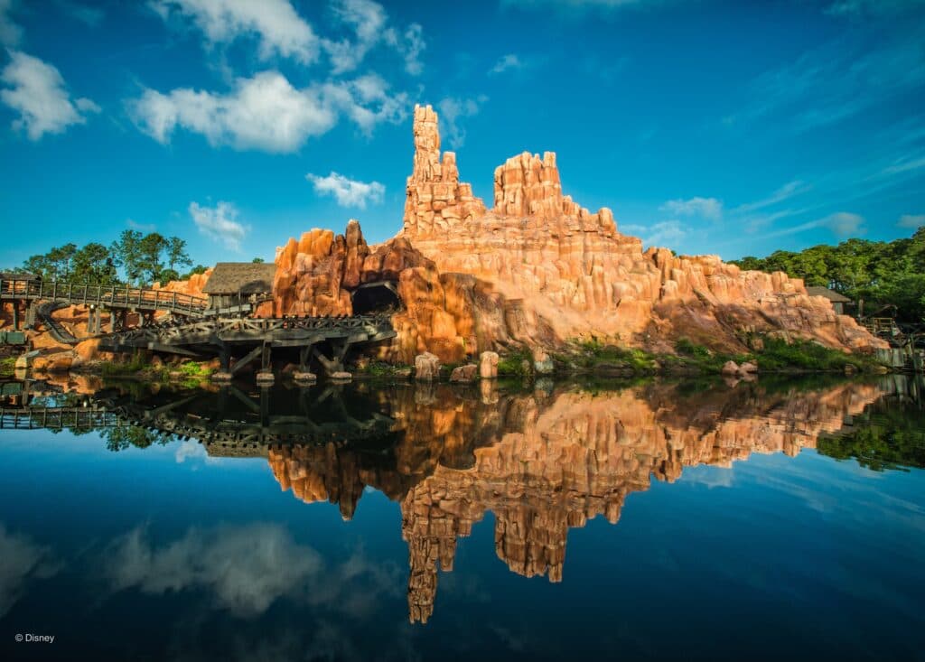 Montanha de mina por onde passa a montanha russa Big Thunder Mountain Railroad com um lindo céu azul que reflete no lago, juntamente com a montanha formando uma imagem espelhada incrível dentro do parque Magic Kingdom que fica em Walt Disney World Resort