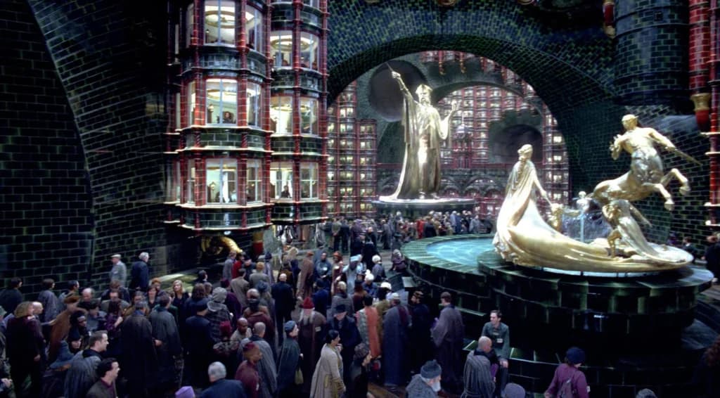 Foto do filme Harry Potter que mostra o ministério da Magia, muito movimentado com muitos aurores e estátuas douradas enormes