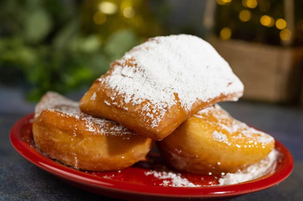 Foto mostra três suculentas Beignets polvilhadas com batante açúcar por cima, doce típico feito pela Princesa Tiana, personagem da Disney, do filme a Princesa e o Sapo.