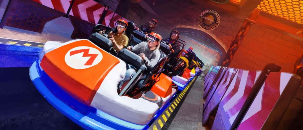 Imagem ilustrativa de como será a nova atração Mario Kart Bowser's Challenge no novo parque da Universal Epic Universal. Mostra pessoas se divertindo sentadas em carrinhos de kart como do jogo Mario Kart, como se estivessem dirigindo e com um óculos 3D em seus olhos