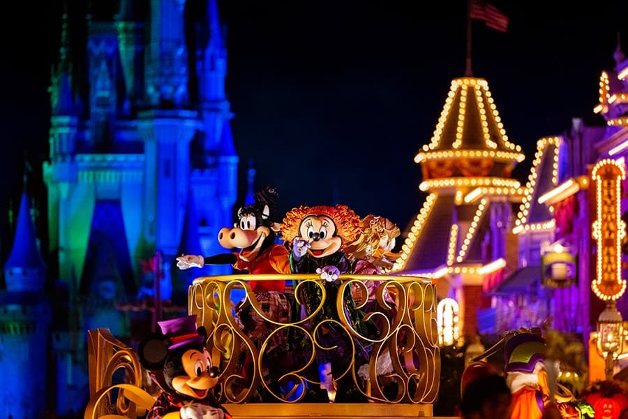 Minnie, Margarida e Clarabela desfilam fantasiadas de irmãs sanderson do filme Hocus Pocus em um carro alegórico durante o desfile de personagens da festa Mickey's not so scary halloween party, que celebra o halloween no parque magic kingdom da disney world. Em frente ao castelo da Cinderela, também é possível ver mais a frente, ainda que fora de foco, o Mickey e o Donald.