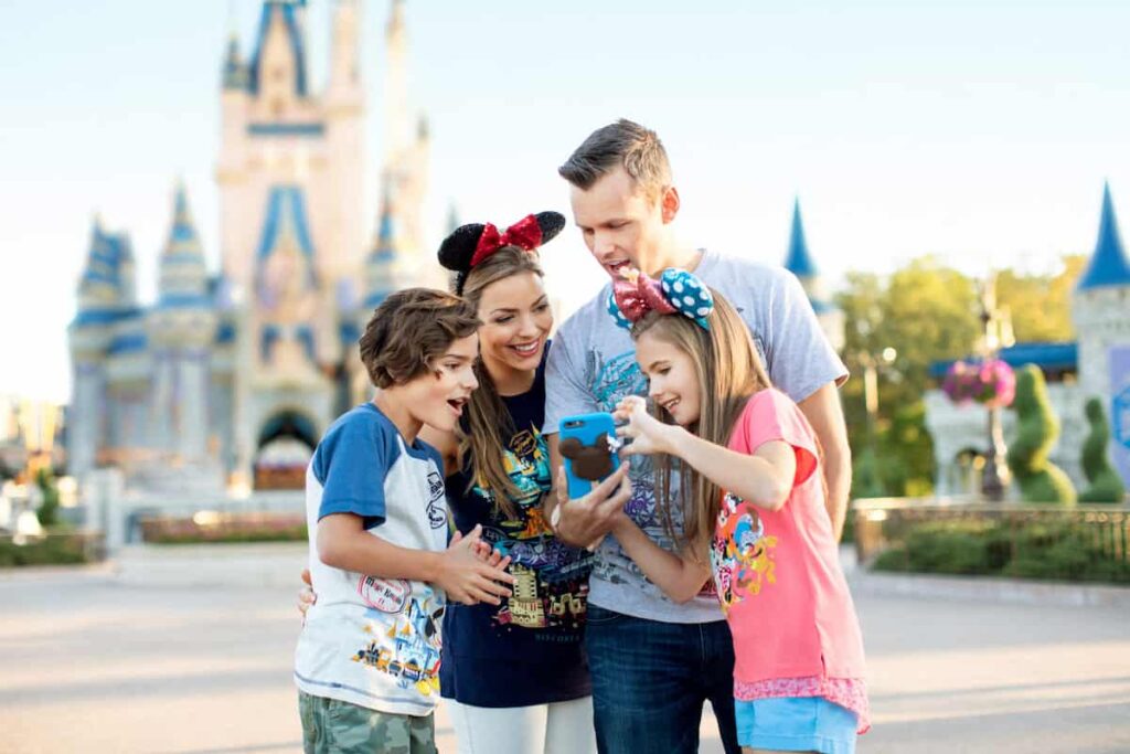 Família composta de uma menina, um menino e um casal de adultos, usa o celular em frente ao castelo da Cinderela no parque Magic Kingdom, em Orlando no Resort Walt Disney World