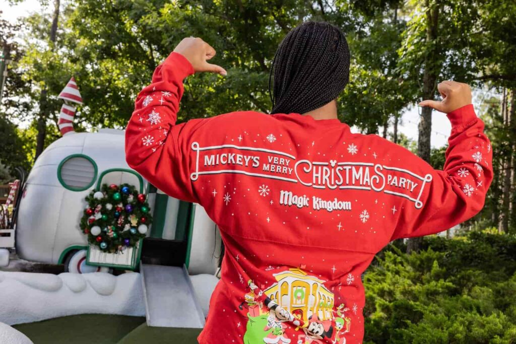 foto mostra Spirit Jersey exclusiva que será comercializada durante a festa de natal do Magic Kingdom na Disney, a Mickey's Very Merry Christmas Party. É um moletom vermelho, sem capuz, e tem o desenho do Mickey e da Minnie em frente Main Street decorada para o natal