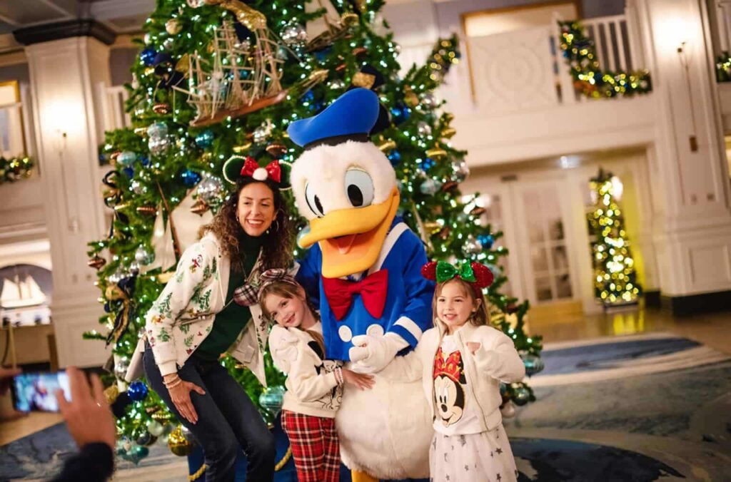 Donald encontra-se para fotos em frente uma árvore de natal em Disney Springs, centro comercial da Disney World, que está totalmente enfeitado para o natal. Duas crianças usando roupas temáticas posam felizes para foto com sua mãe e o personagem