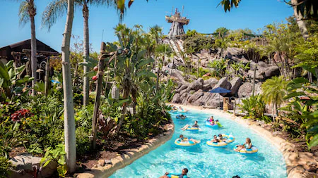 Foto área do parque aquático Disney's Typhoon Lagoon, que mostra bem ao fundo o barco que ficou preso no alto por causa do tufão que atingiu a região, trazendo a história do parque a vida, e a frente temos um rio lento onde as pessoas boiam e se divertem