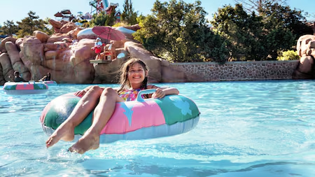 Menina em uma bóia rosa e verde água com detalhes azuis se diverte no parque aquático da Disney