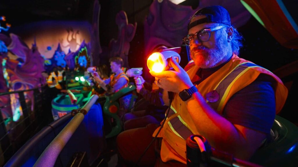 imagineer, engenheiro da disney, está a frente da foto, segurando o blaster usado para atirar nos alvos na atração Buzz Lightyear Ranger Spin, que estará em reforma para atualização em 2025