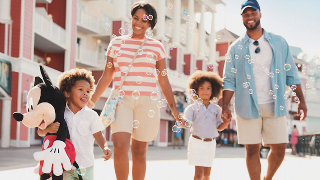 família composta de casal e duas crianças, anda junta e feliz pelo Disney's Boardwalk, sendo que uma das crianças segura uma pelúcia do Mickey e todos estão muito animados, indicando que estão tendo férias incríveis em Walt Disney World