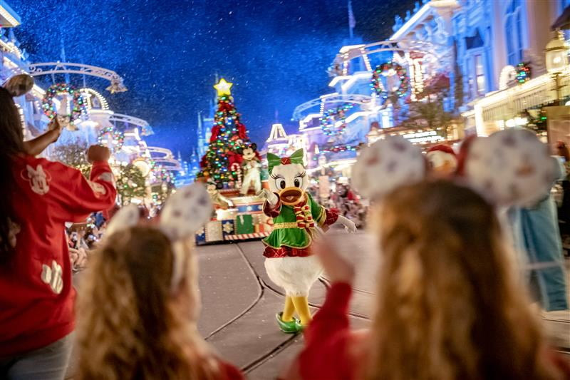 Foto da Margarida, vindo frente ao carro alegórico de natal do Mickey e da Minnie com sua árvore de natal, passando pela rua principal do parque Magic Kingdom durante a festa especial de natal Mickés Very Merry Christmas Party