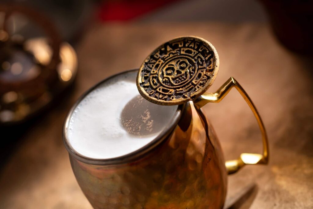 foto de caneca estilo moscow mule, com uma moeda pirata com uma caveira, a bebida cursed treasure, que estará disponível no novo bar pirata estilo pub Beak and Barrel no Magic Kingdom