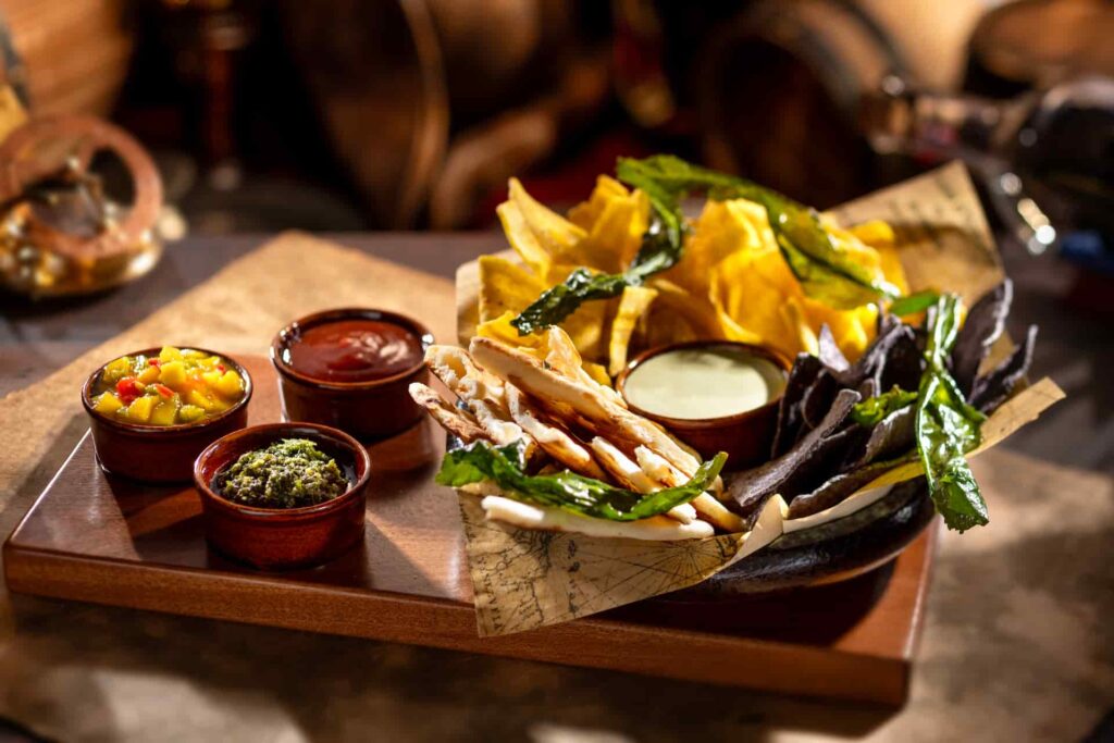 um dos pratos de petiscos, o island provisions, que estará disponível no novo bar Beak and Barrel na Disney, dentro do parque de diversões Magic Kingdom, é possível ver uma cesta com vários tipos de chips e molhos
