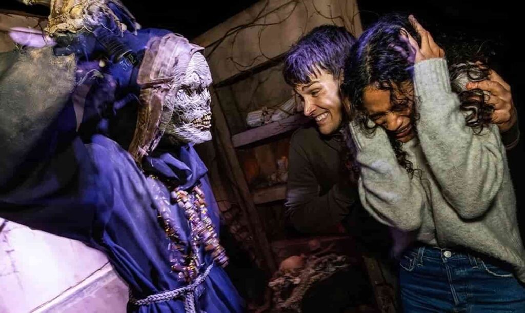 foto de divulgação da festa Halloween Horror Nights da Universal Orlando 2025 onde podemos ver um pessoa sorrindo para um monstro e outra completamente assustada com as mãos na cabeça, tapando os ouvidos e olhos fechados