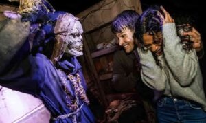 foto de divulgação da festa Halloween Horror Nights da Universal Orlando 2025 onde podemos ver um pessoa sorrindo para um monstro e outra completamente assustada com as mãos na cabeça, tapando os ouvidos e olhos fechados