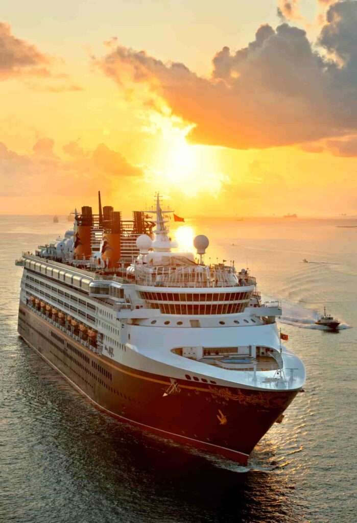 Navio da Disney Cruise Line navega em alto mar sob um lindo por do sol alaranjado com algumas nuvens no céu