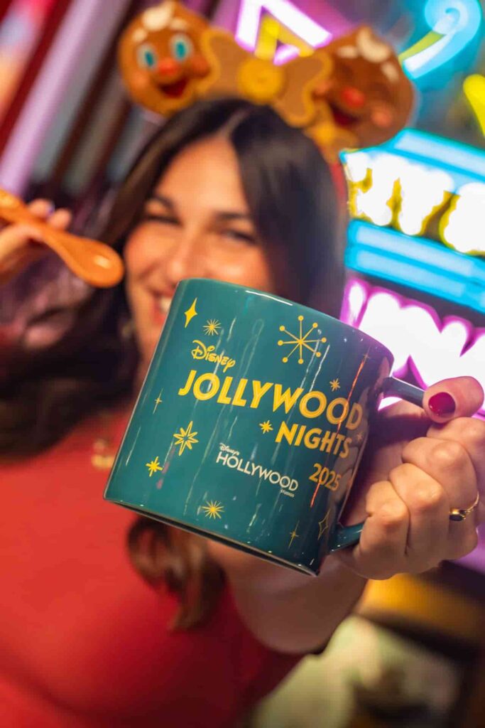 Mulher de orelhinhas da Minnie, em frente ao teatro chinês, na atração Mickey e Minnie Runaway Railway, exibe a caneca da festa Jollywood Nights, a festa de Natal do parque temático Hollywood Studios na Disney