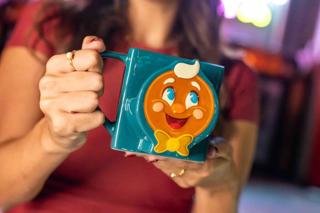 Mulher em frente ao teatro chinês, na atração Mickey e Minnie Runaway Railway, exibe a caneca da festa Jollywood Nights, a festa de Natal do parque temático Hollywood Studios na Disney