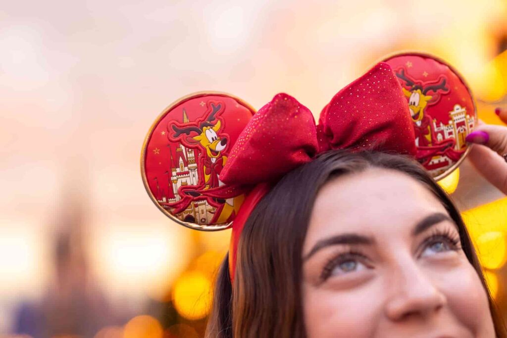 Mulher feliz exibe suas orelhinhas da Minnie temáticas da festa de Natal Mickey's Very Merry Christmas Party que é totalmente vermelha e tem renas do Papai Noel como decoração