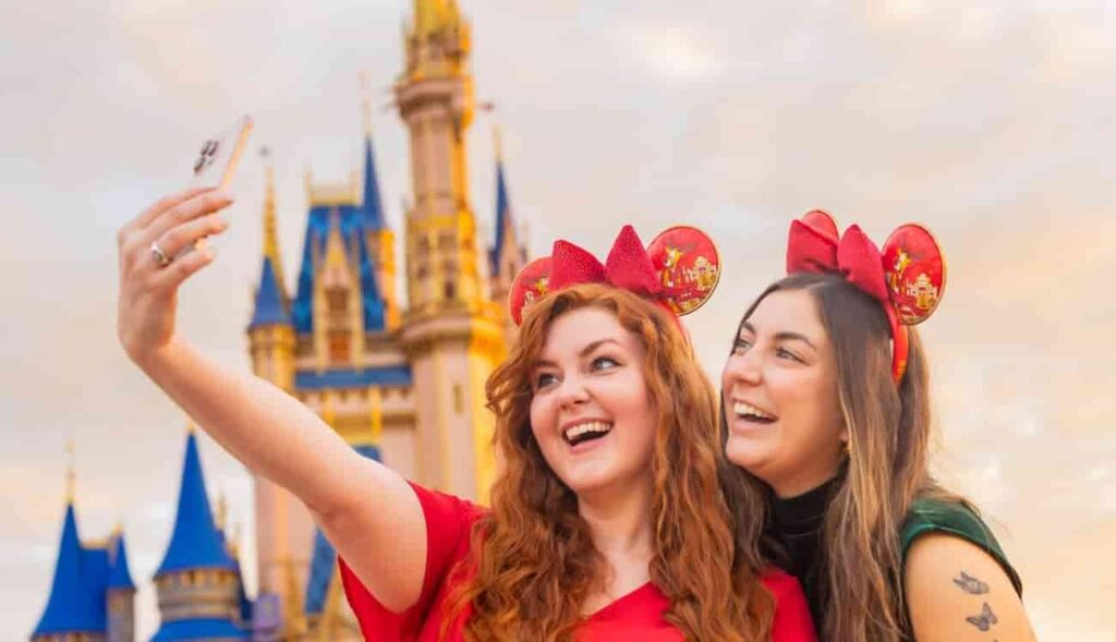 Mulheres felizes sorriem e posam para selfie em frente ao iconico Castelo da Cinderela no Magic Kingdom, parque temático em Walt Disney World Resort Orlando, usando orelinhas da Minnie Mouse temáticas da Festa de Natal Mickey's Very Merry Christmas Party