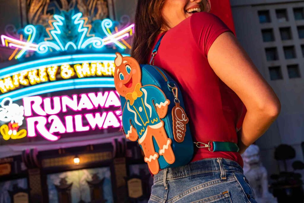 Mulher de costas virando para mostrar sua mochila Loungefly de gingerbread, simbolo da festa natalina da Disney no Hollywood Studios, a Jollywood Studios, em frente ao teatro chinês, na entrada do parque