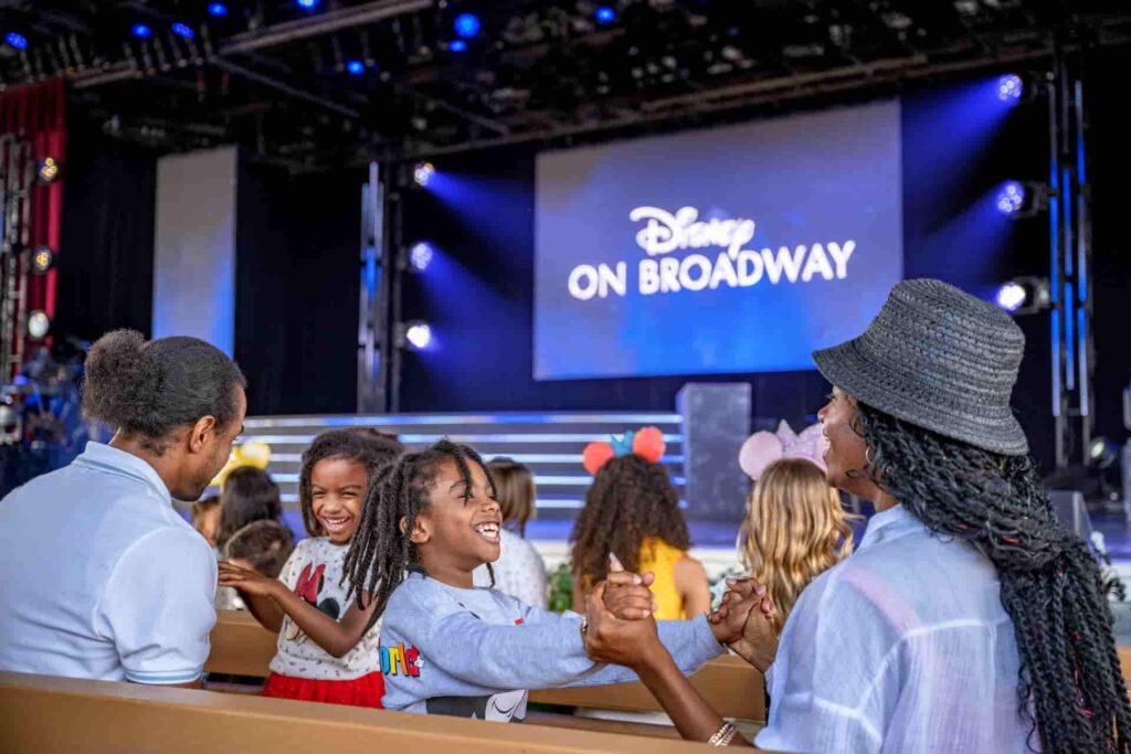 Visitantes sentados interagem uns com os outros enquanto aguardam o começo do show Disney on Broadway que acontece no Epcot
