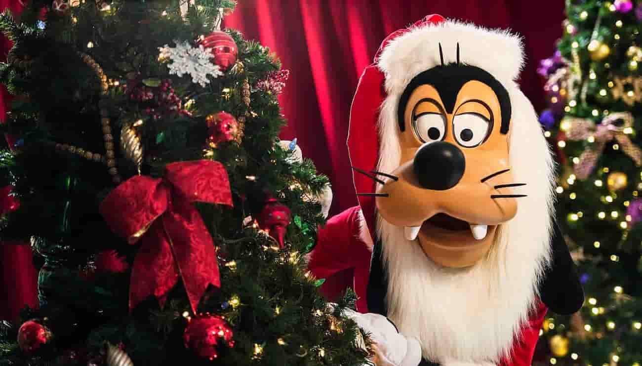 Pateta vestido de Papai Noel se esconde atrás de uma árvore de natal na Disney
