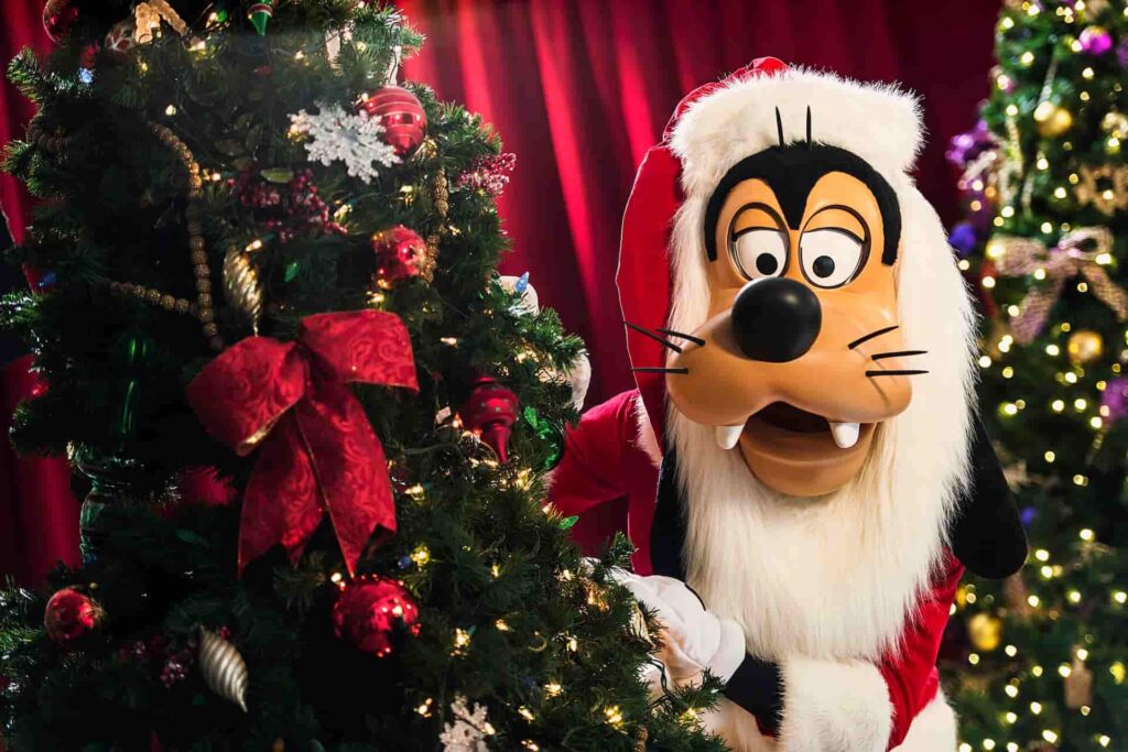 Pateta vestido de Papai Noel se esconde atrás de uma árvore de natal na Disney