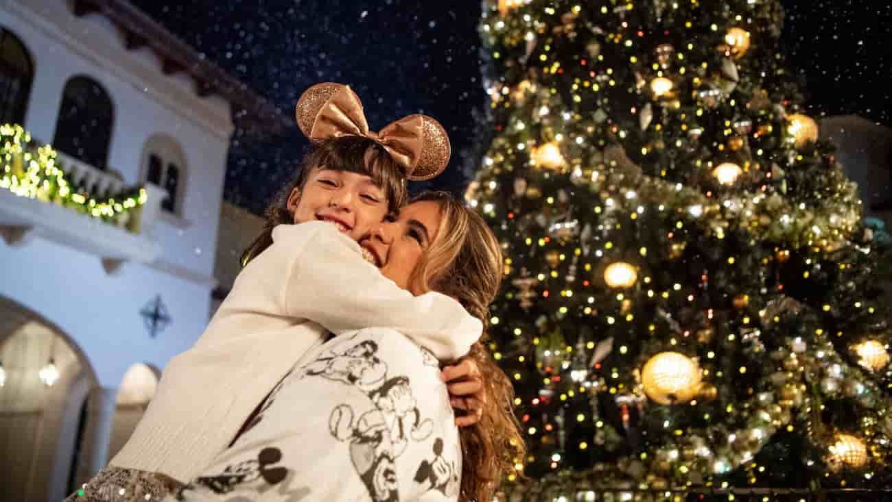 Mãe e filha se abraçam e curtem a neve em frente uma árvore de natal durante as festas de final de ano no Disney Springs
