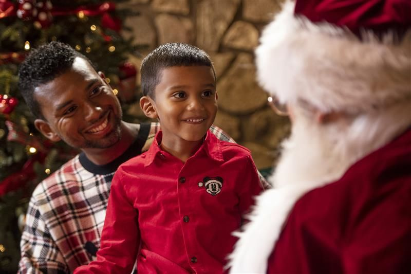 Menininho acompanhado de seu pai encontra com Papai Noel durante as festas de final de ano no Disney Springs