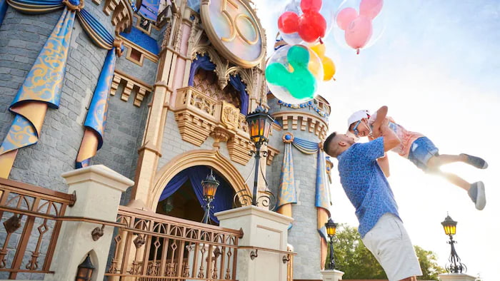 Homem brinca levantando seu filho no ar em frente ao Castelo da Cinderela com balões da Disney no parque de diversões Disney's Magic Kingdom