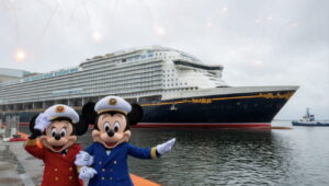 Capitão Mickey junto a Capitã Minnie posam felizes e sorridentes para foto em frente ao novo navio da frota da Disney Cruise Line, o Disney Adventure