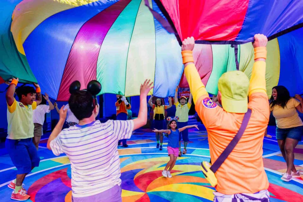 adultos e crianças se divertem ao brincar e dançar no GoofyCore, dentro do Epcot, onde podem encontrar o Pateta durante o verão