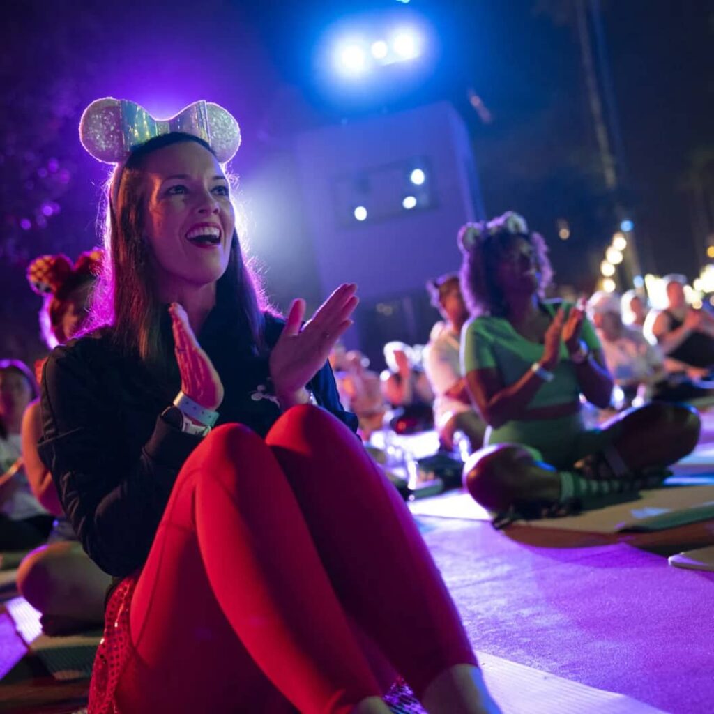 Mulheres com roupas de ginástica sentadas em tapete de de yoga e usando orelhinhas da Minnie aplaudem apresentação especial do evento