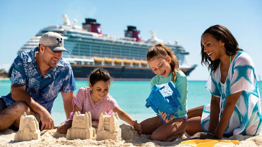 Familia brinca na areia da praia fazendo castelinhos de areia na Castaway Cay a ilha particular da Disney proximo ao navio da Disney Cruise Line