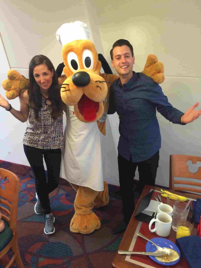 Casal posa para foto com o Pateta no restaurante Chef Mickey's que tem café da manhã e jantar com personagens
