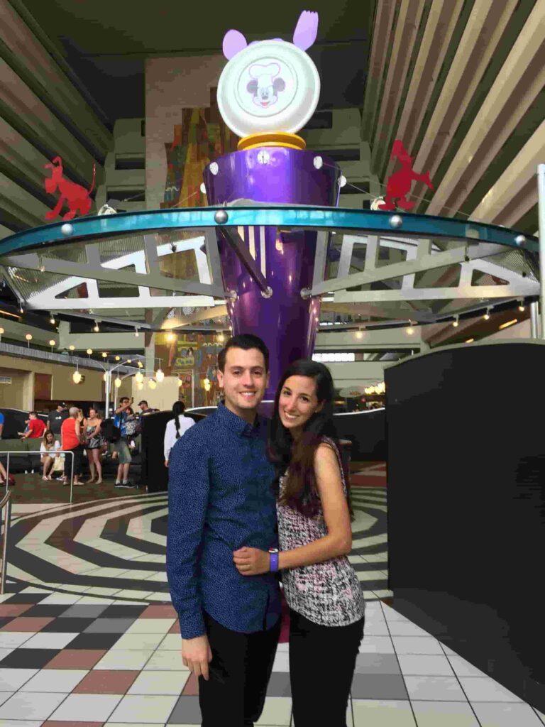 Casal posa na entrada do restaurante Chef Mickey's que tem café da manhã e jantar com personagens