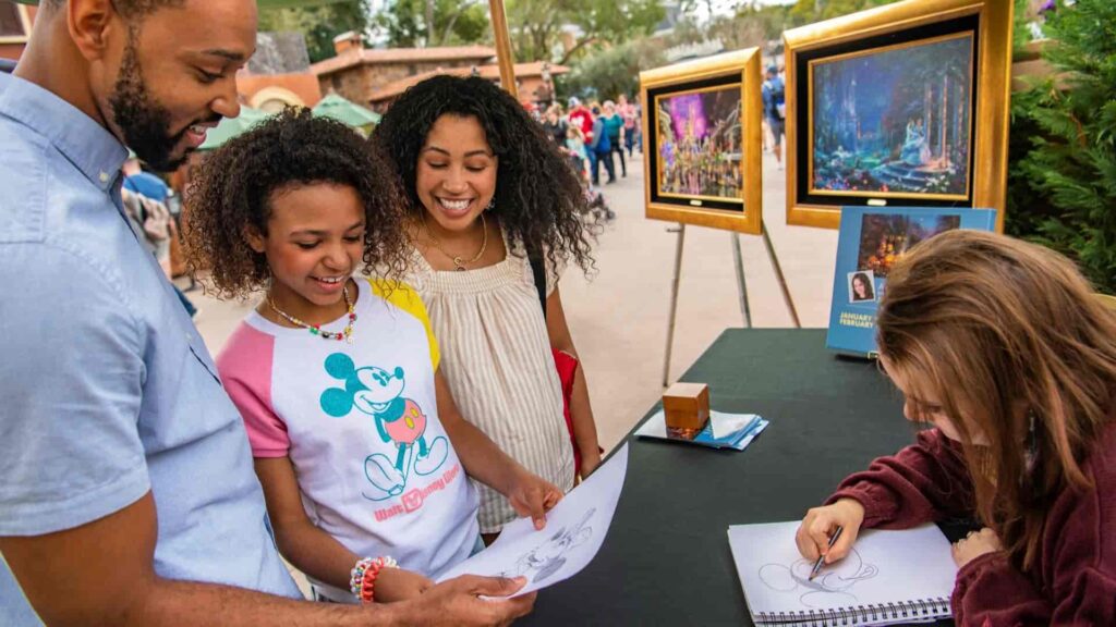 Criança se encanta com desenho do Mickey junto aos seus pais enquanto completa pintura no Epcot durante o Festival of The Arts que acontece anualmente na Disney World