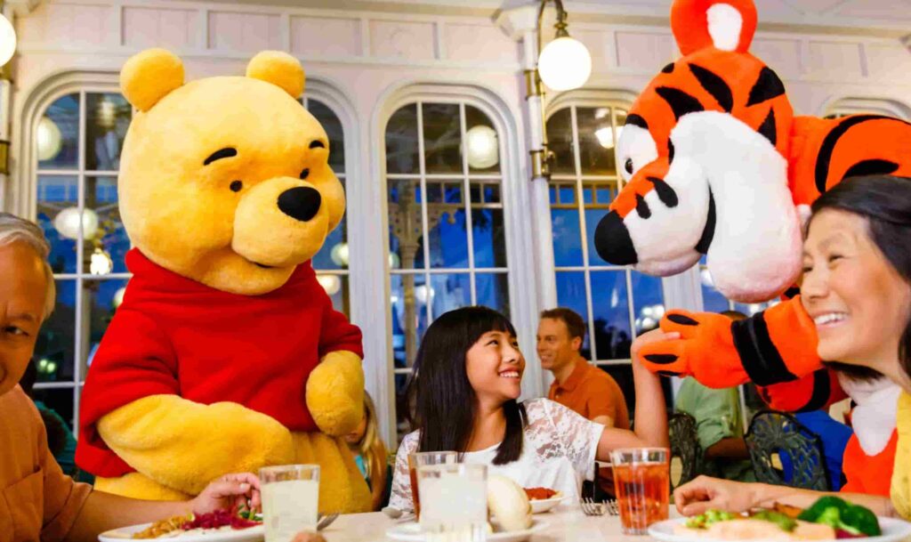 Personagens Pooh e Tigrão interagem com família na mesa do restaurante Crystal Palace onde é possível encontrar o Ursinho Pooh e seus amigos durante refeições no café da manhã, almoço e jantar