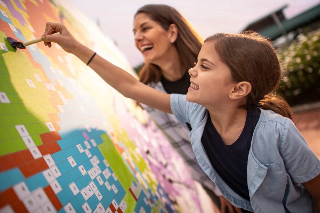 Criança se diverte com sua mãe enquanto completa pintura em quadro colaborativo no Epcot durante o Festival of The Arts que acontece anualmente na Disney World