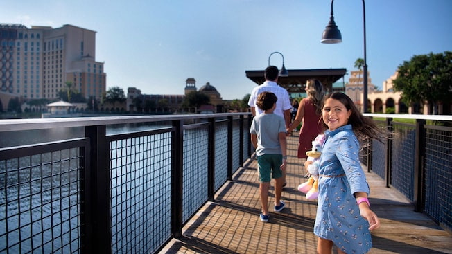 Familia anda na ponte do hotel Disney's Coronado Springs e a menina, que segura uma pelúcia da Margarida, olha para trás sorrindo