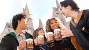 Amigos vestidos com robes de Hogwarts brindam felizes com suas canecas de buterbeer, a cerveja amanteigada uma das bebidas mais tradicionais da Universal, inspirada no Wizarding World of Harry Potter