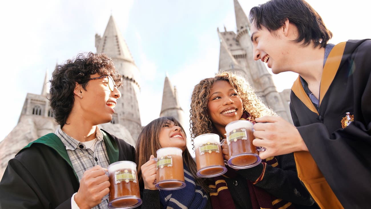 Amigos vestidos com robes de Hogwarts brindam felizes com suas canecas de buterbeer, a cerveja amanteigada uma das bebidas mais tradicionais da Universal, inspirada no Wizarding World of Harry Potter