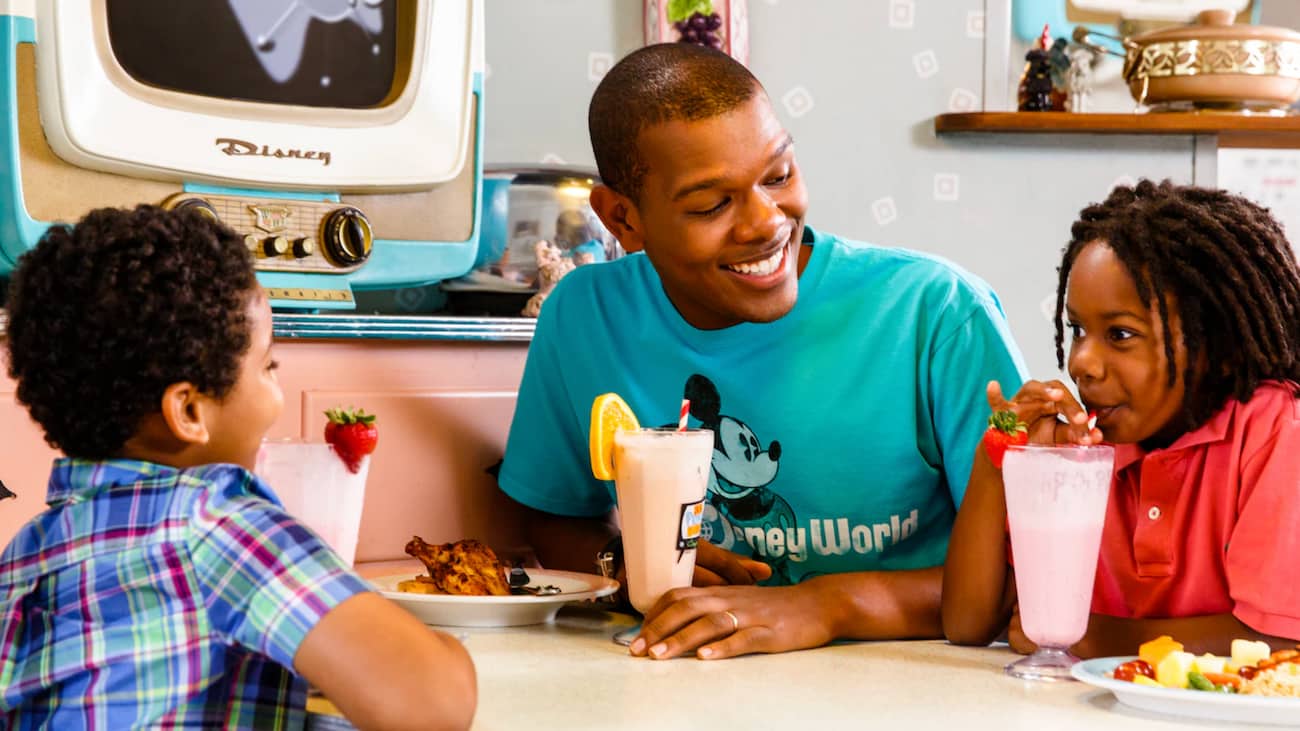 Pai se diverte com filhos tomando milk shake durante refeição no restaurante 50's prime time da Disney no parque Hollywood Studios em Orlando