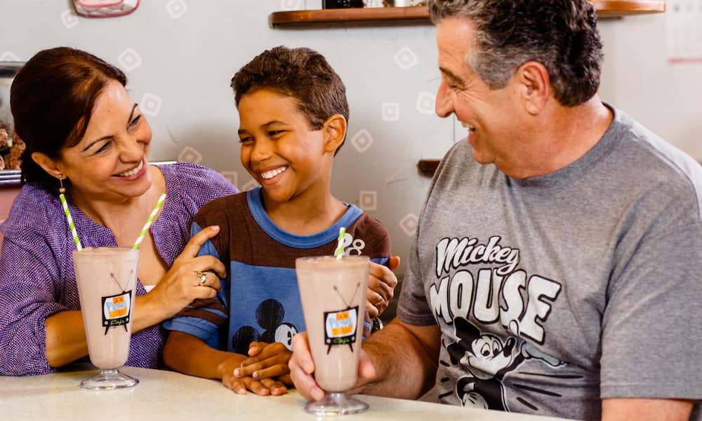 Pais se diverte com filhos tomando milk shake durante refeição no restaurante 50's prime time da Disney no parque Hollywood Studios em Orlando