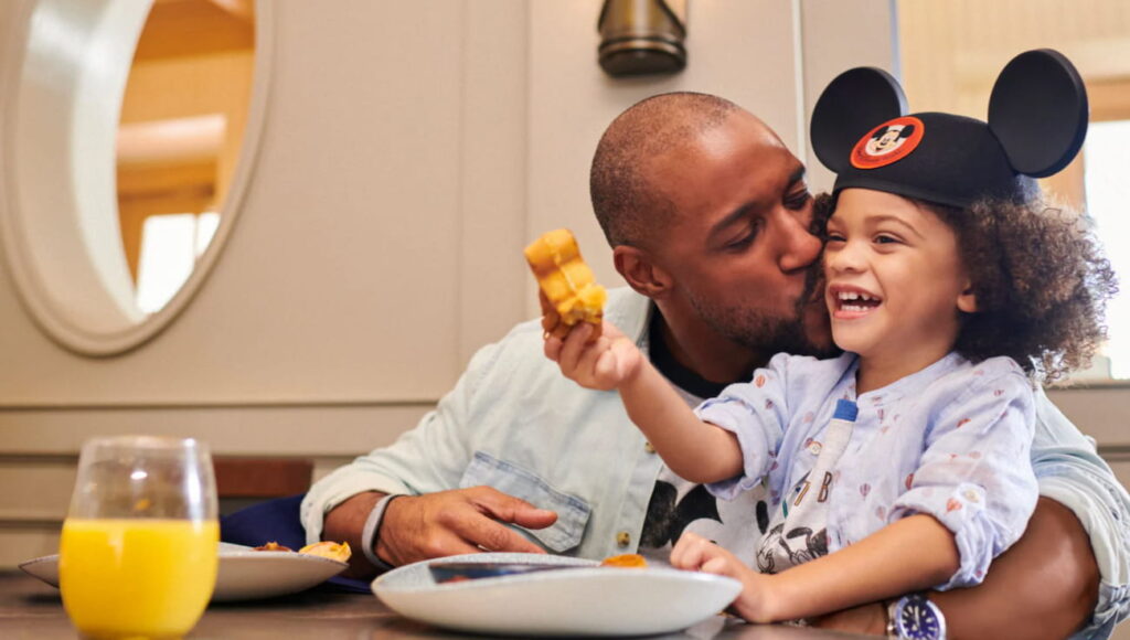 Pai e filho trocam momento de carinho e diversão enquanto comem waffle do Mickey no restaurante Ale & Compass no hotel Disney's Yatch Club na Disney World