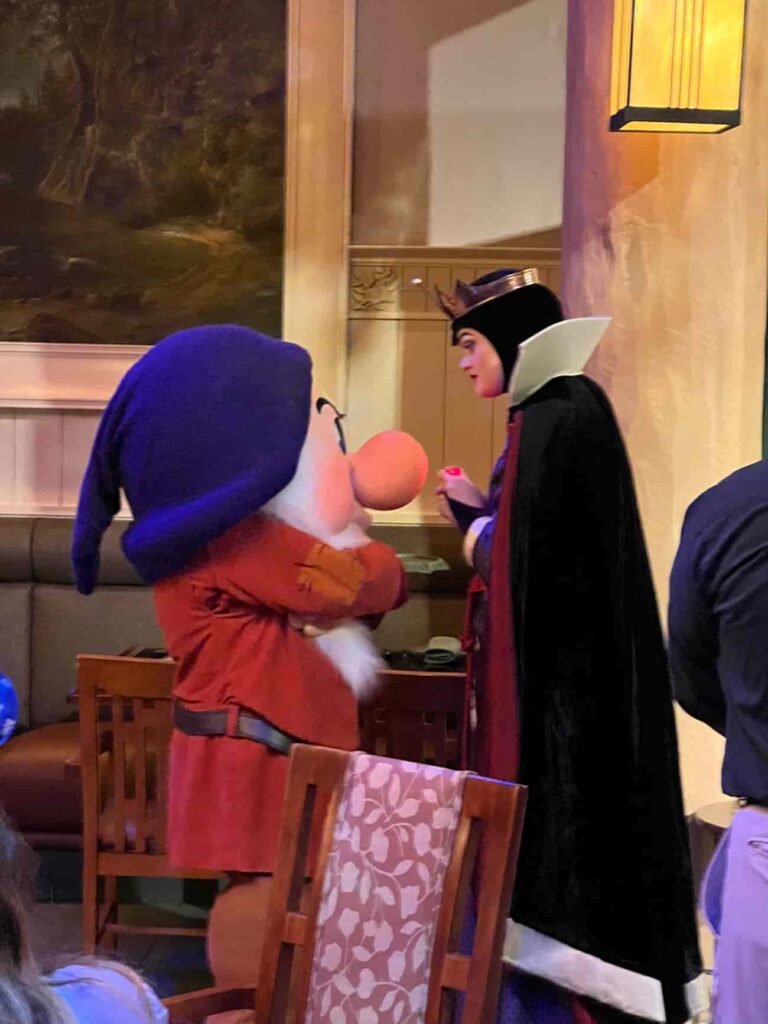 Rainha Má interage com Zangado durante refeição no Storybook Dining at Artist Point, restaurante com personagens no Wilderness Lodge que conta com Zangado, Dunga, Branca de Neve e Rainha Má