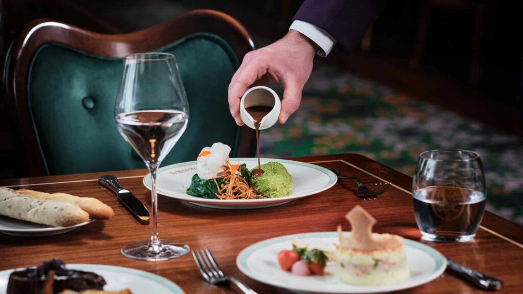 Garçom serve molho na comida que está posta sobre a mesa no restaurante Regal View and Lounge na Disneyland Paris