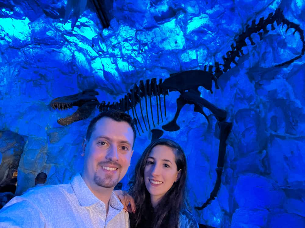 Casal posa em frente a um esqueleto de dinossauro congelado dentro do restaurante T-Rex em Disney Springs