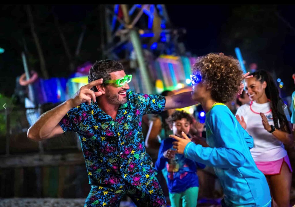 Pai e filho dançam e se divertem no evento noturno H2O Glow que acontece em noites selecionadas no verão americano entre junho e setembro no parque aquático de Walt Disney World Resort, o Typhoon Lagoon
